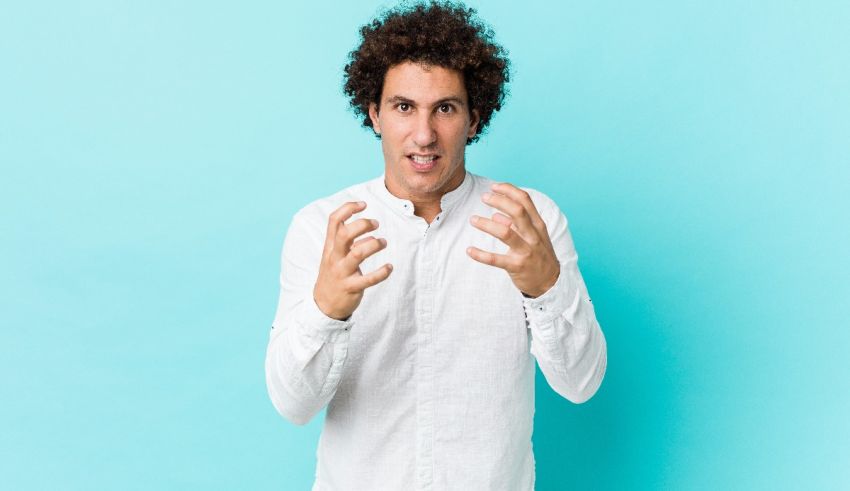 A man with curly hair making a gesture against a blue background.