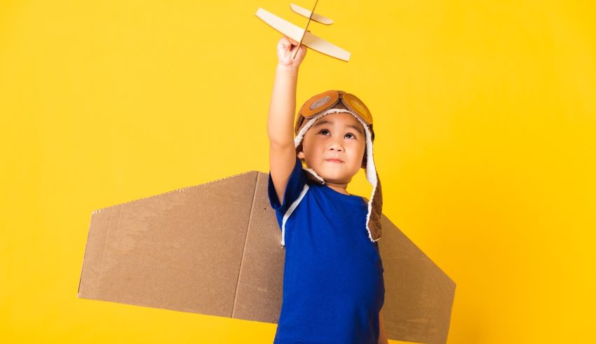 A boy is holding up a cardboard airplane on a yellow background.