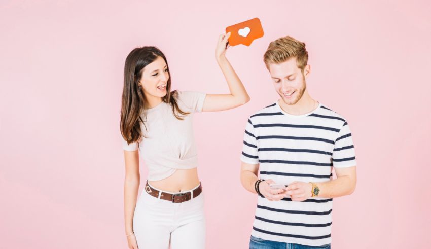 A man and a woman are holding up a mobile phone over a pink background.