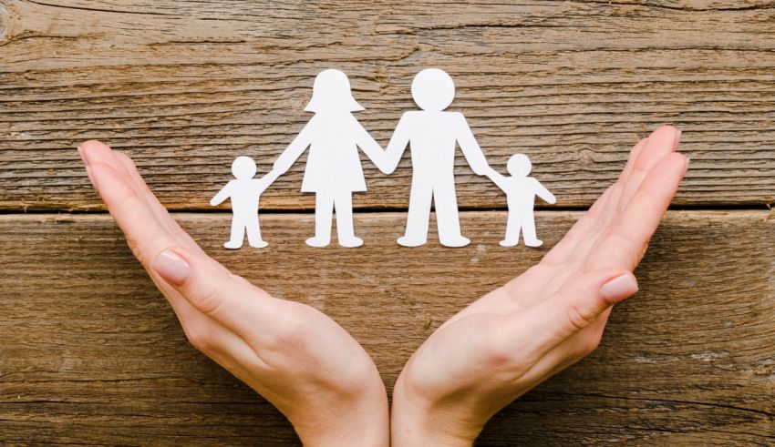 A woman's hands holding a paper cut out of a family on a wooden background.