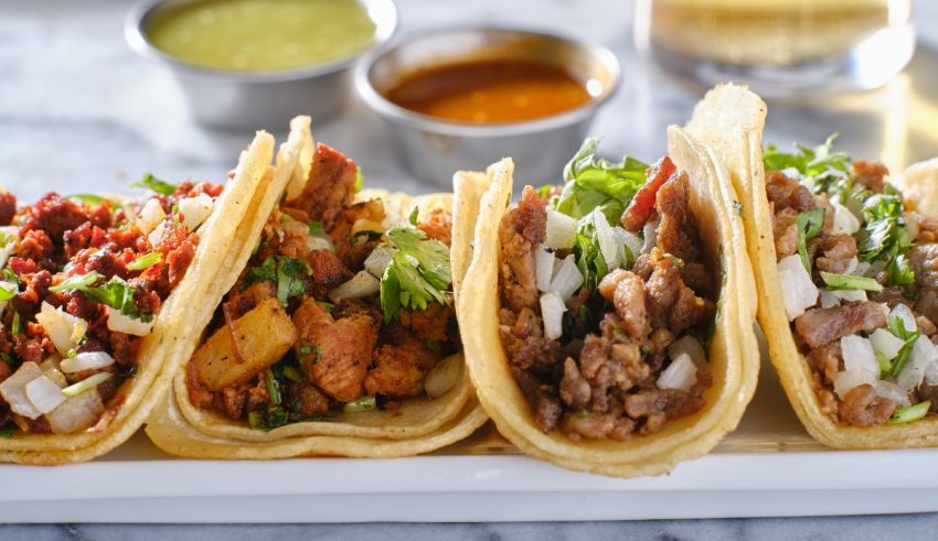 Four tacos are sitting on a white plate.