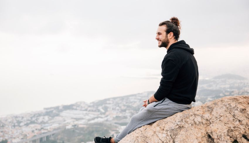 A man sitting on top of a mountain looking at the city.