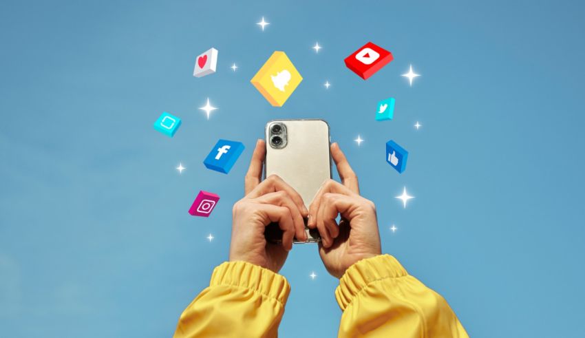A hand holding a phone with social icons flying around it.