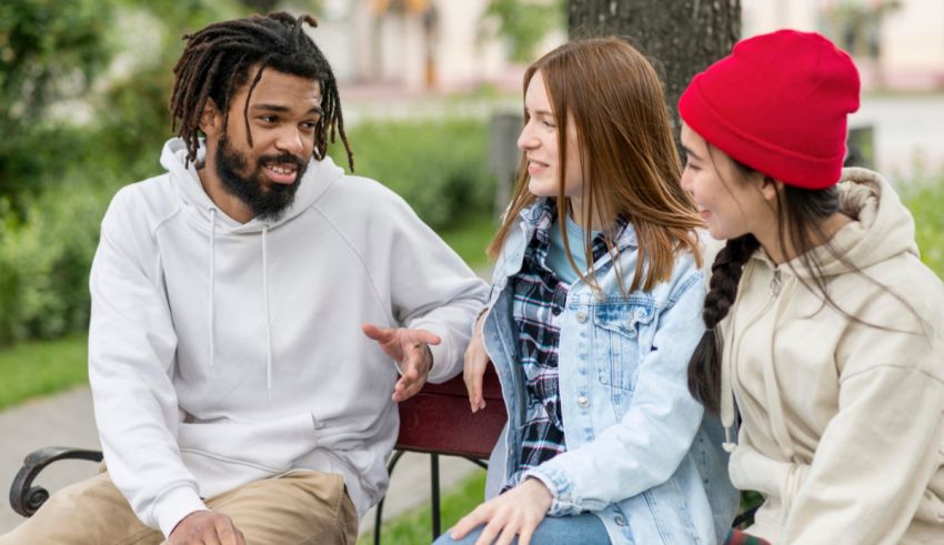 Three young people sitting on a bench talking to each other.