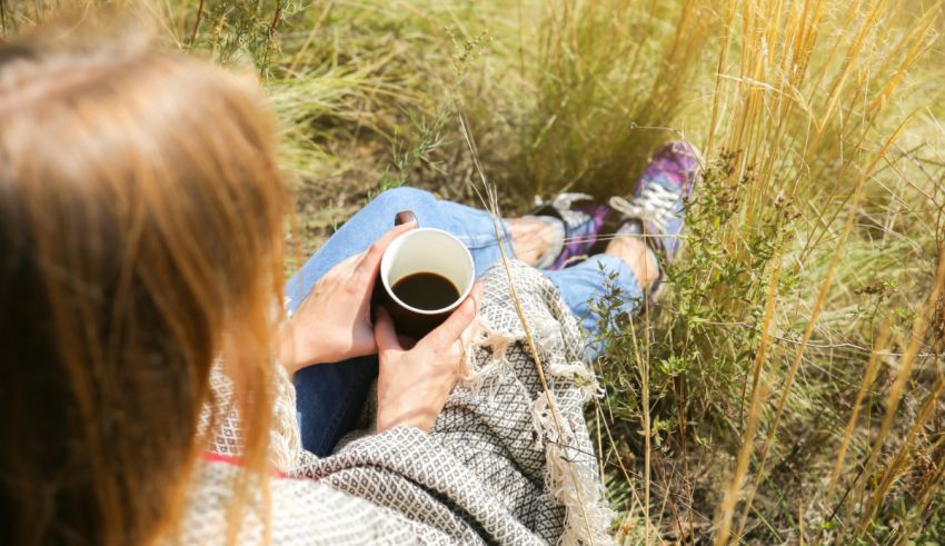 A woman is sitting in a field with a cup of coffee.