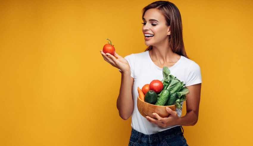 A young woman holding a bowl of vegetables on a yellow background.