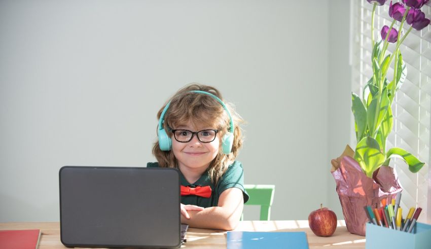 A little girl wearing headphones is using a laptop.