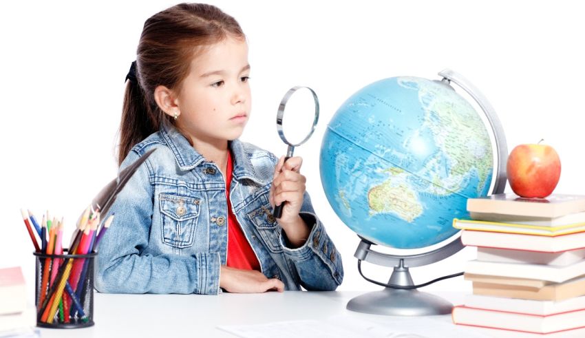 A little girl looking at a globe with a magnifying glass.