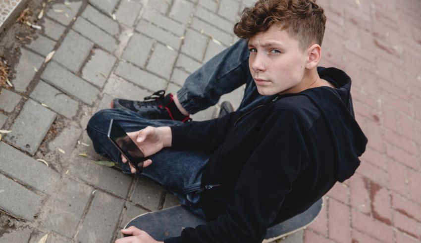 A boy sitting on a skateboard looking at his phone.