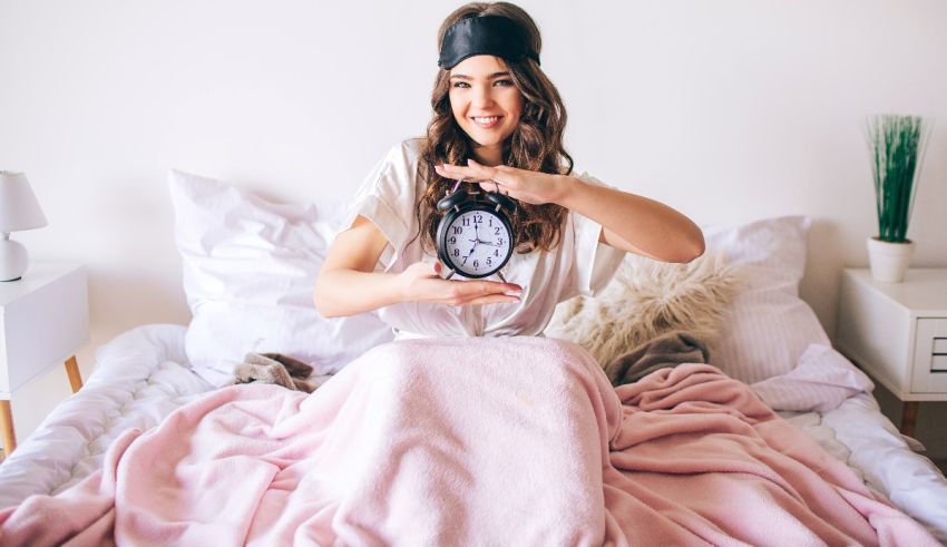 A young woman holding an alarm clock in bed.