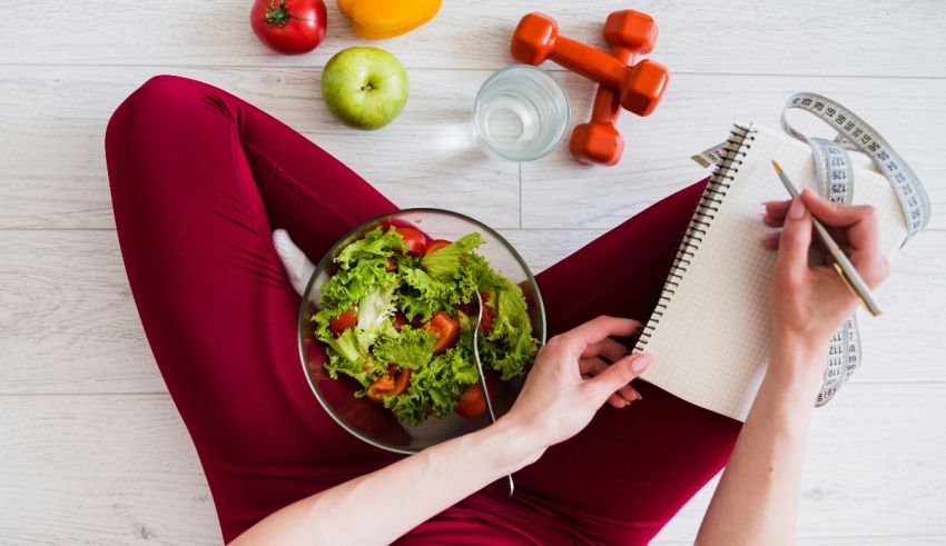 A woman is holding a notebook while eating a salad.