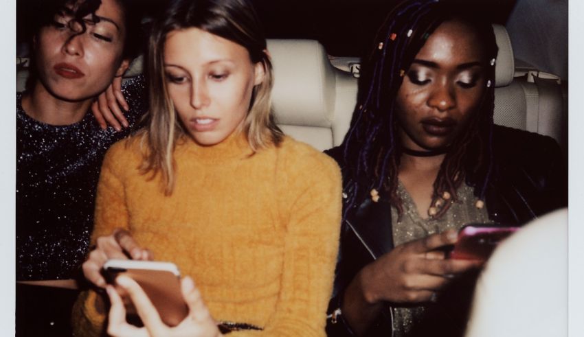 Three women sitting in a car looking at their cell phones.