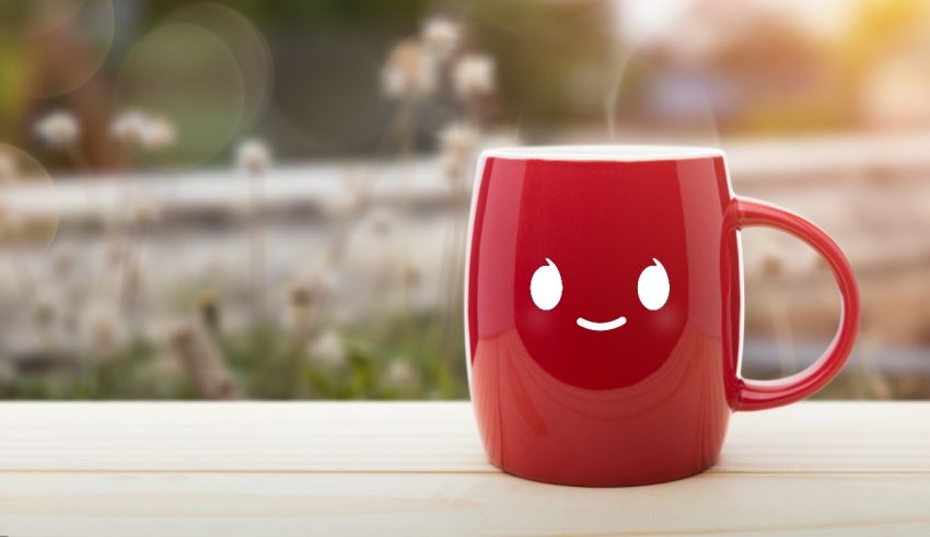 A red mug with a smiley face on it sits on a wooden table.