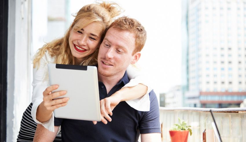 A man and woman hugging each other while looking at a tablet computer.
