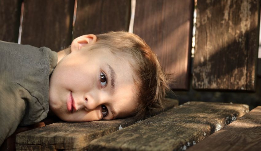 A young boy laying on a wooden bench.