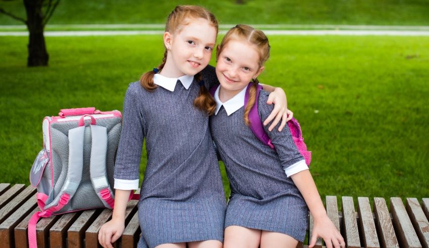 Two girls in school uniforms sitting on a bench.