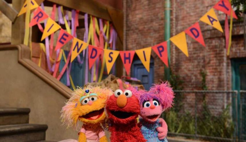 Elmo, person, person, and person pose for a photo in front of a banner.