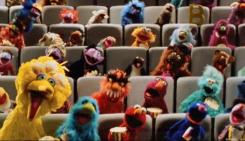 A large group of sesame street characters are sitting in a theater.