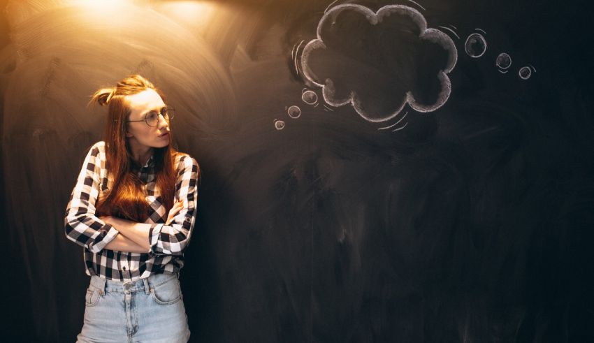 A young woman standing in front of a chalkboard with a thought bubble.