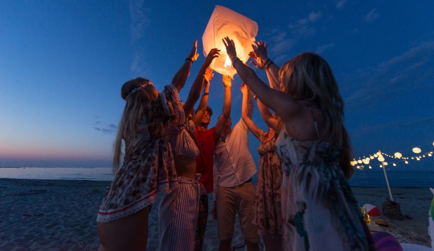A group of people holding up a paper lantern on the beach.
