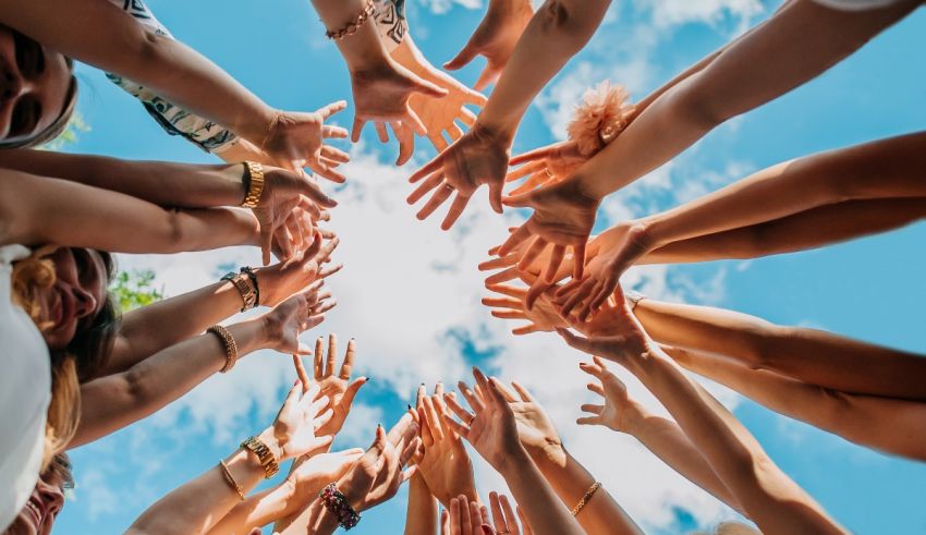 A group of hands forming a circle with a blue sky background.