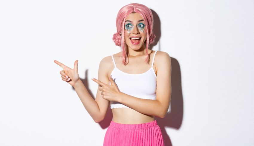 A young woman with pink hair pointing to the camera.