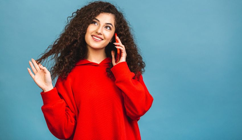 A young woman is talking on the phone in a red sweater.