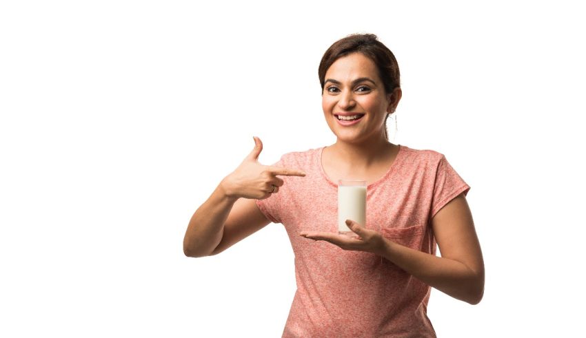 A woman holding a glass of milk and showing the thumbs up.