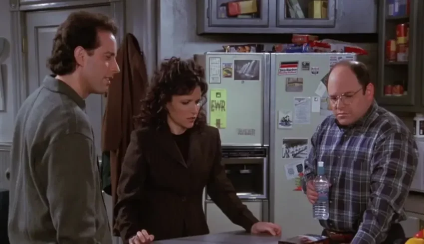 Three people standing in a kitchen with a refrigerator.