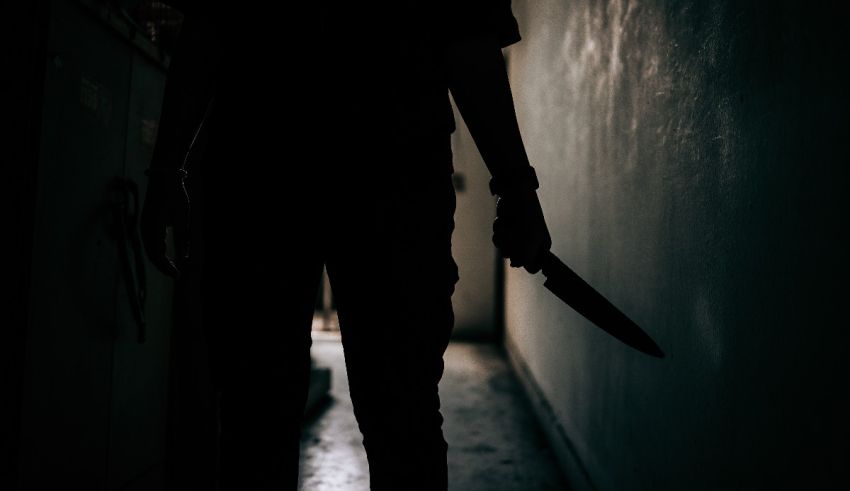 A silhouette of a person holding a knife in a dark hallway.