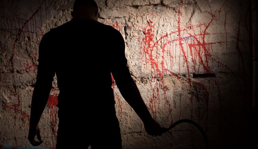 A silhouette of a man holding a scythe in front of a wall with blood on it.