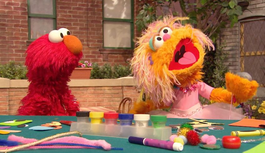 Two sesame street characters are sitting at a table making crafts.