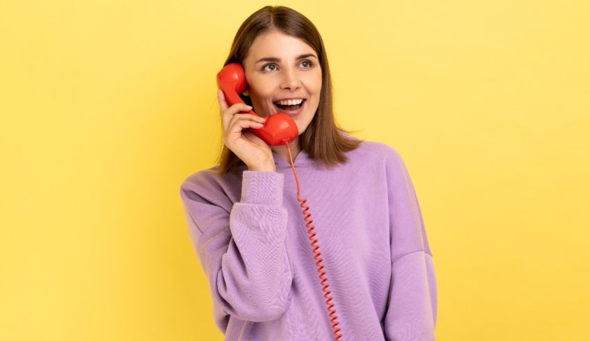 A young woman talking on a red phone against a yellow background.