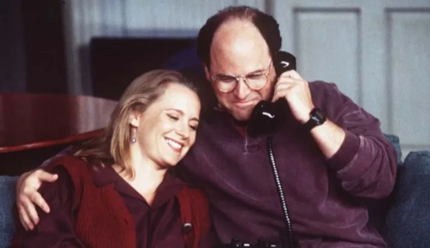 A man and woman sitting on a couch talking on the phone.