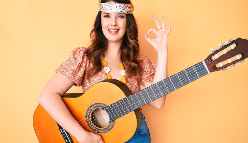 A woman holding an acoustic guitar and making the ok sign.
