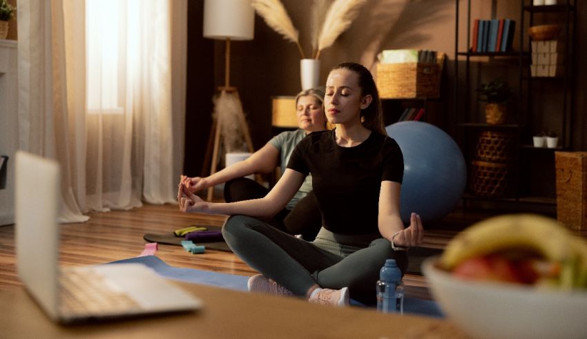 Two women meditating in front of a laptop in a living room.