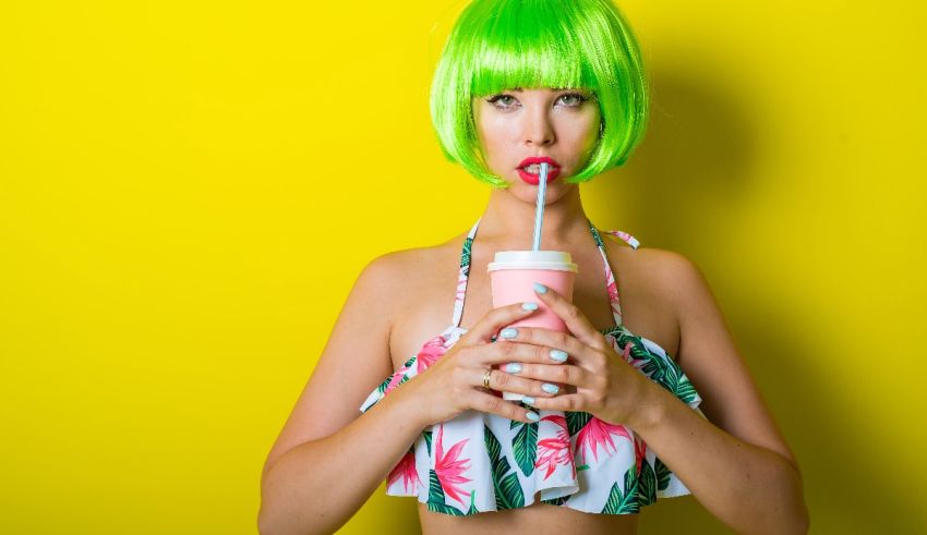 A woman with green hair drinking a drink on a yellow background.