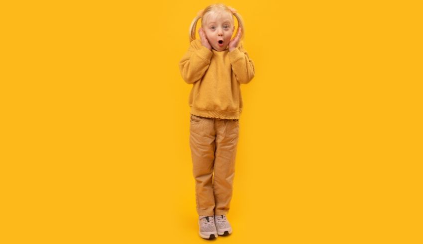 A little girl in a yellow sweater is standing on a yellow background.