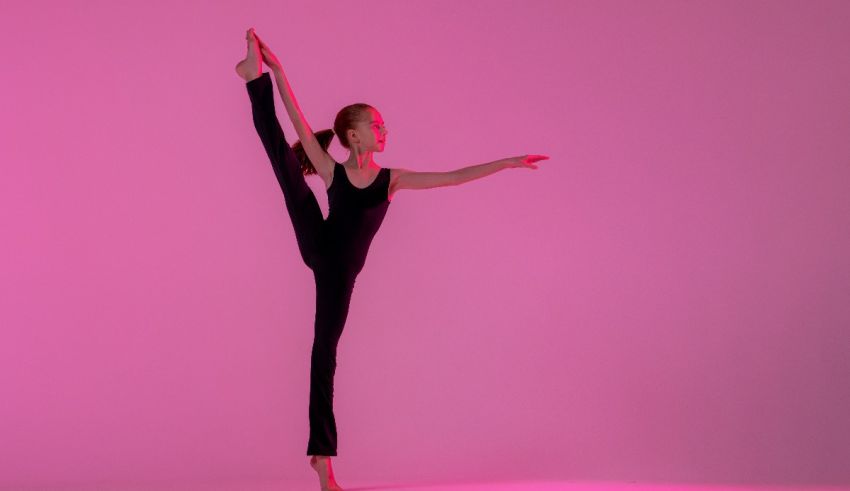 A young dancer is doing a split pose on a pink background.