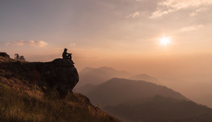 A man sitting on top of a mountain at sunset.