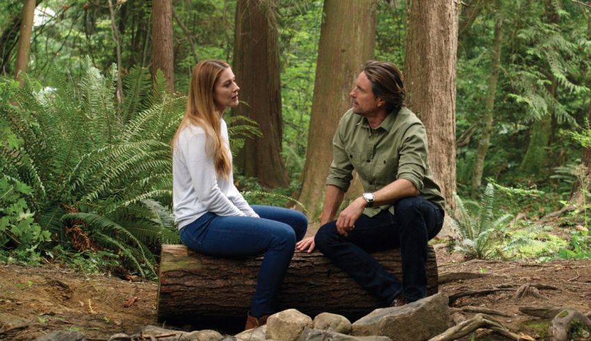 A man and woman sitting on a log in the forest.