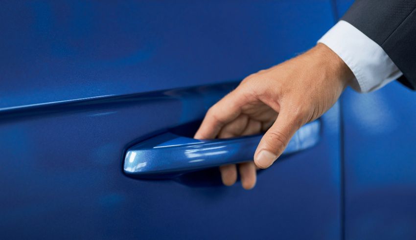 A man is opening the door handle of a blue car.