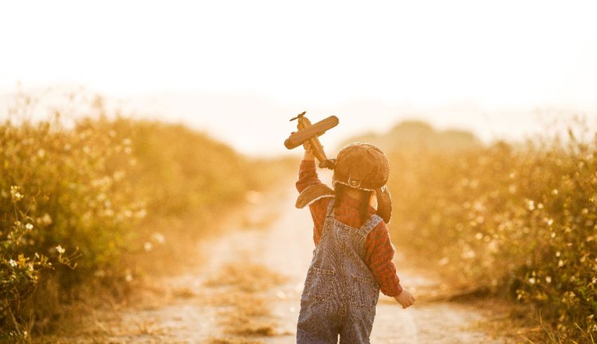 A child is walking down a dirt road holding a toy airplane.