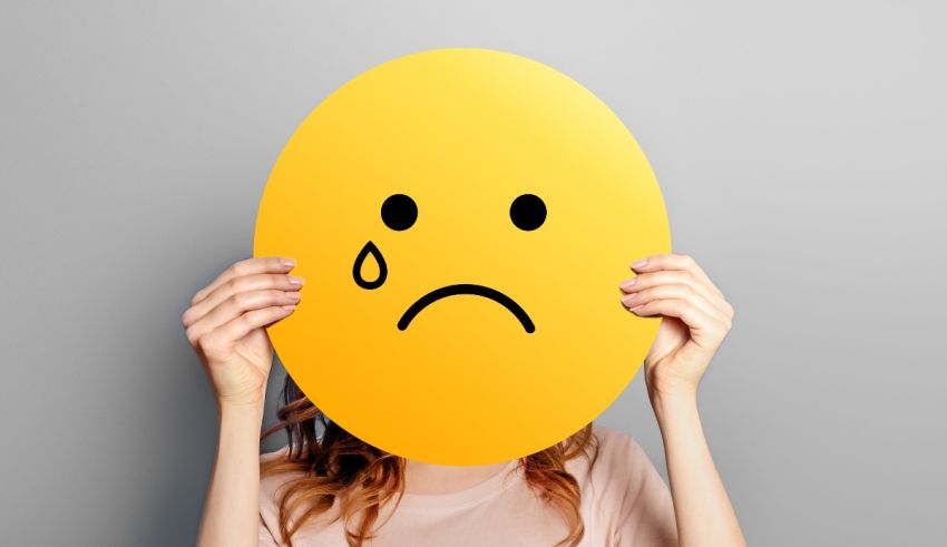 A woman holding a yellow sad emoticon over her face.