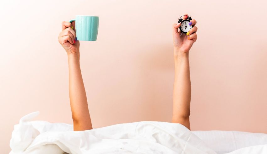 A woman is laying in bed with a cup of coffee.