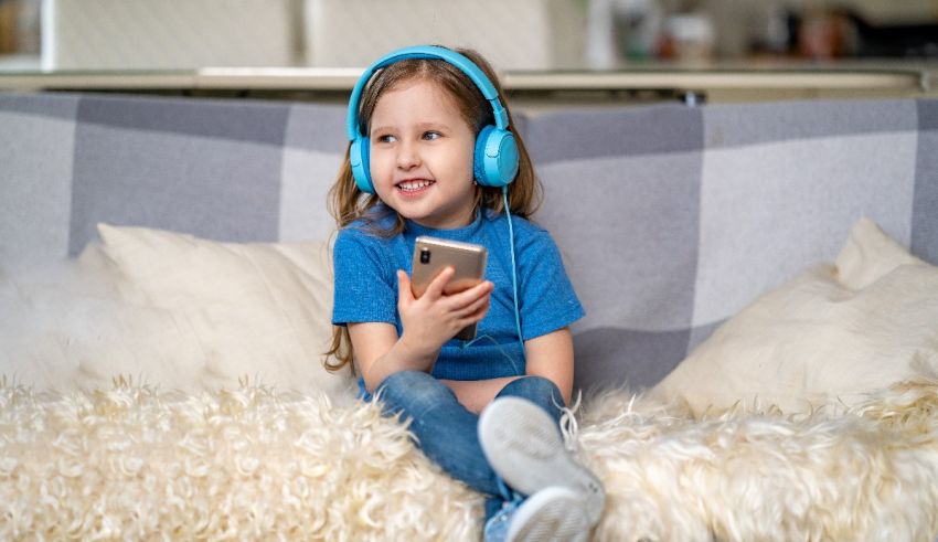 A little girl sitting on a couch with headphones listening to music.