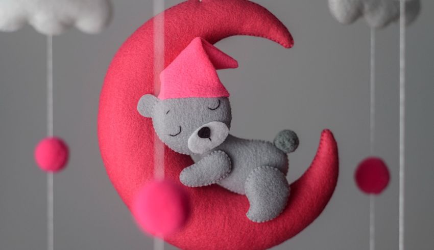 A felt teddy bear sleeping on a pink crescent.
