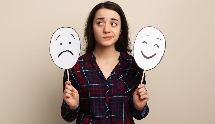 A young woman holding up two paper faces with sad and happy expressions.