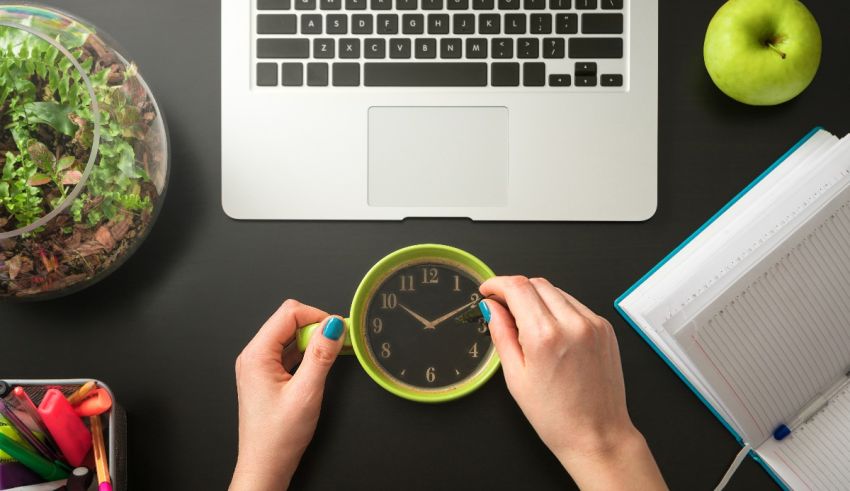 A woman's hands are holding a clock next to a laptop.