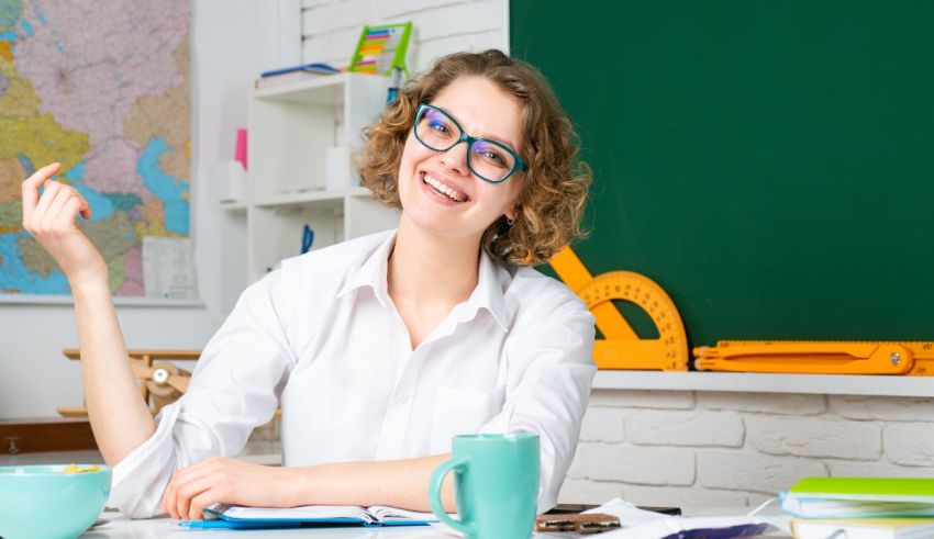 A girl in glasses is sitting at a desk with a cup of coffee.